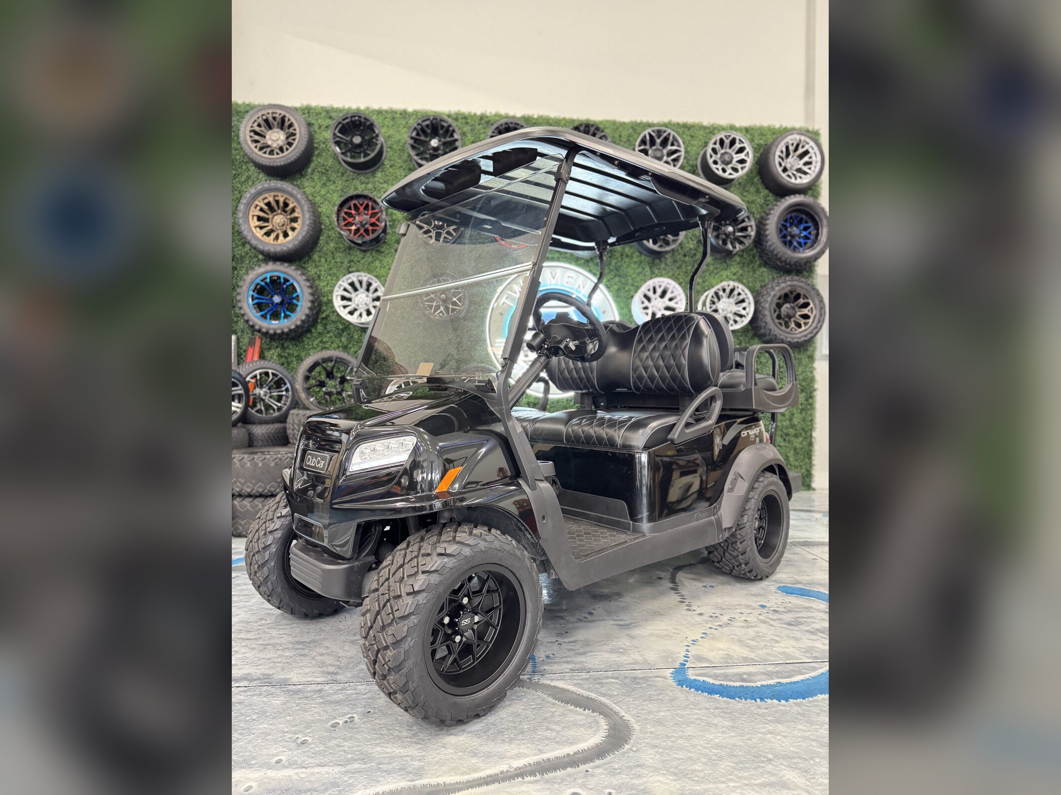 All-black Club Car Onward in front of custom wheel display wall