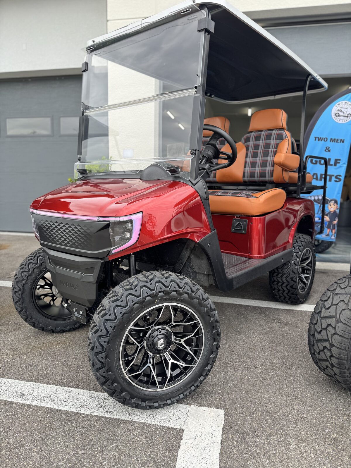 Candy red lifted MadJax X-Series with saddle leather and tartan plaid seats outside the shop